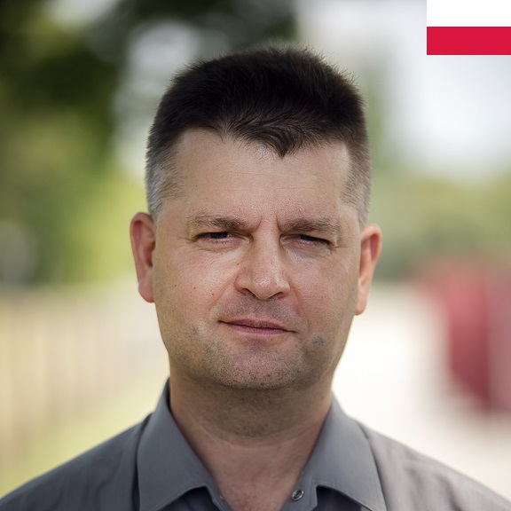 Portretowe zdjęcie mężczyzny. W prawym górnym rogu ikona biało-czerwona flaga Polski