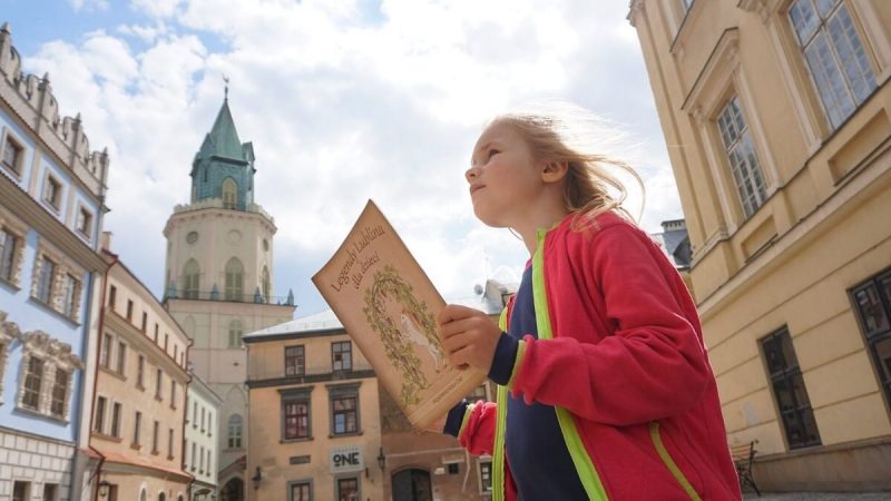 Dziewczyna z ksiażką o lubelskich legendach na tle Wieży Trynitarskiej